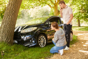 couple next to car crashed into tree inspecting accident damage and calling emergency services